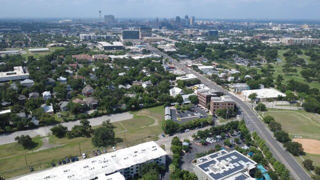 Observation tower rises beyond Broadway Mahncke Park in South Texas tree canopy. Solar panel arrays border dense neighborhood greenery, multi family residences, open green lawns, San Antonio
