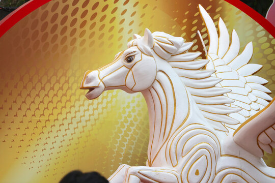Close-up side view of a white Pegasus statue with gold outlines against a golden graphic background.