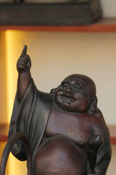 Close-up of a carved wooden Laughing Buddha statue pointing a finger up against a warm blurred background.