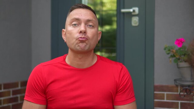 Highly engaging commercial ready video of a funny man spitting cherry pits directly into the camera on a house porch.