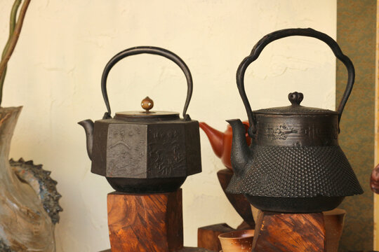 Two vintage cast iron teapots displayed on wooden stands against a beige wall.