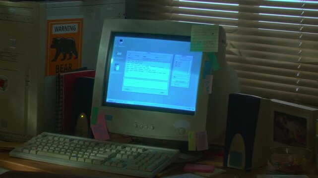 Handheld shot of retro computer setup on desk with CRT monitor displaying old operating system interface, camera zooming in. Ideal for nostalgic technology documentaries or retro marketing campaigns