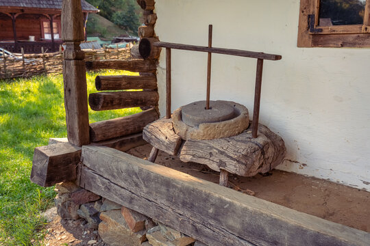 Traditional stone hand mill on a rustic porch beside an old rural house in Romania