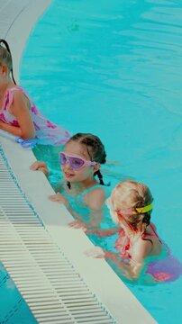 Young girls gather at pool edge wearing swimming goggles. Concept of group swimming lessons, water safety, social interaction, childhood friendship and active recreation.