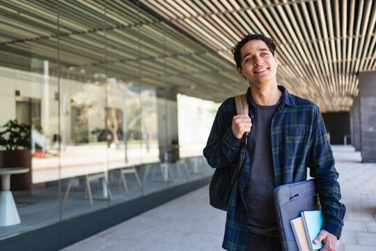 Smiling hispanic university student walking along of college campus hallway