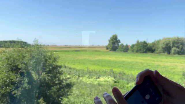 Woman photographs passing countryside from a different train window angle as camera pans to view in slow motion. Concept of digital lifestyle and capturing travel memories during business journey.