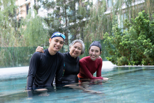 Happy multigenerational family relaxing together in a swimming pool after aquatic activity, smiling at the camera while expressing healthy aging, togetherness, active living, and lasting wellness.