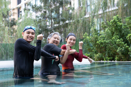 Smiling family celebrating together in a swimming pool after aquatic exercise, showing strength poses that reflect healthy aging, active lifestyle, support across generations, and wellness.