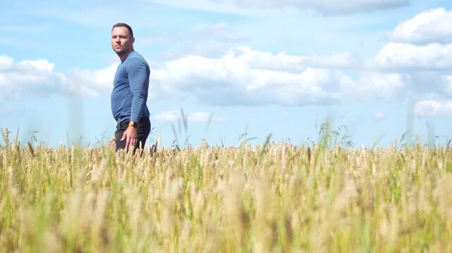 Athletic male traveler enjoying freedom and a country lifestyle, floating his hands over a cereal crop field under a blue sky with white clouds.