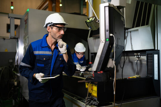 A factory technician monitors CNC machine operation while holding a clipboard inside a manufacturing facility. The image represents industrial automation, production monitoring, and workplace safety