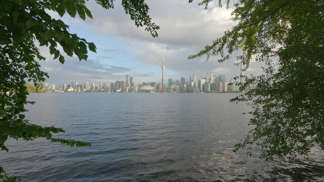 Toronto skyline viewed from Centre Island through surrounding trees, with calm water in the foreground and the city stretching across the horizon.