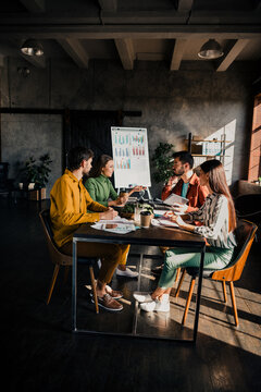 Young team collaborating in a modern office around a table during a business meeting with charts and laptops on a flipchart presentation