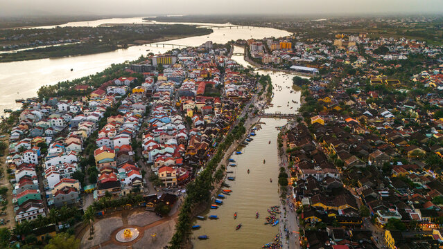 Aerial view of the historic Hoi An Ancient Town with its traditional yellow buildings, tiled rooftops, and bustling riverfront boats in Hoi An, Da Nang, Vietnam.