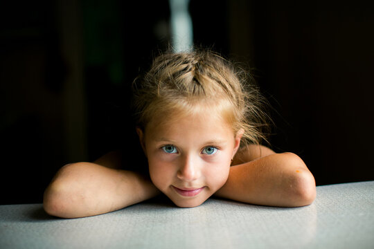 Close up portrait of a young girl resting her head on folded arms and looking at the camera indoors