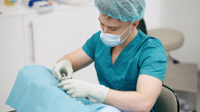 Surgeon in scrubs, mask, and gloves performing a delicate medical procedure using surgical instruments on a patient