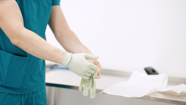 Medical professional wearing teal scrubs putting on a sterile surgical glove in a hospital setting, ensuring hygiene and patient safety