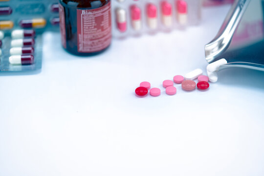 Red, pink, and white tablets pills with drug tray on blurred glass drug bottle and blister pack. Cracked tablets pills. Expired drugs. Painkiller medicine. Pharmacy shop. Pharmaceutical industry.