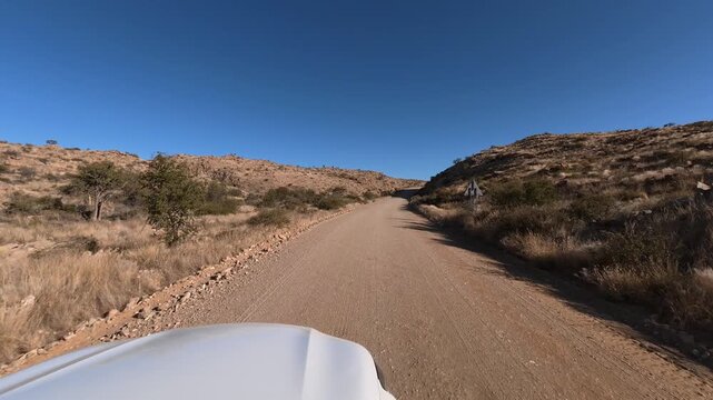 A lone white car drives along a dusty dirt road in Namibia, Africa.