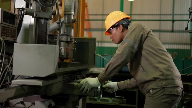 Industrial worker operates a machine in a manufacturing factory while wearing protective equipment, representing machine operation, production, engineering, and workplace safety.