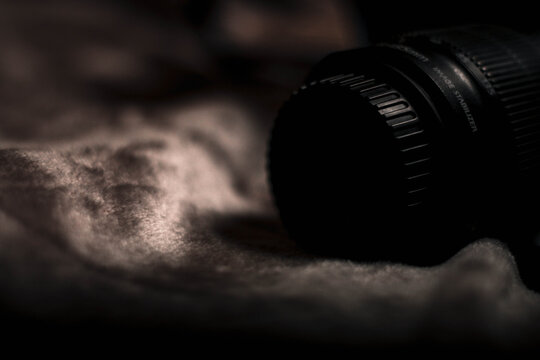 A close-up of a camera lens resting on a soft, dark textured fabric in moody lighting