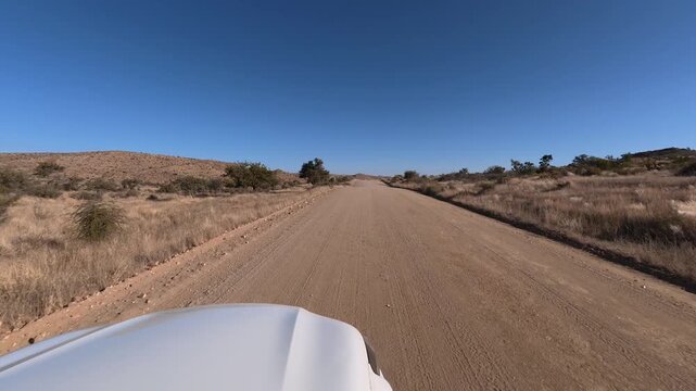 A lone white car drives along a dusty dirt road in Namibia, Africa.