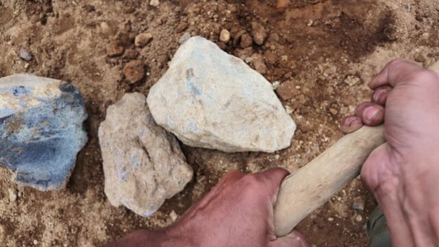 Hand hammering rock on dirt ground hard work.