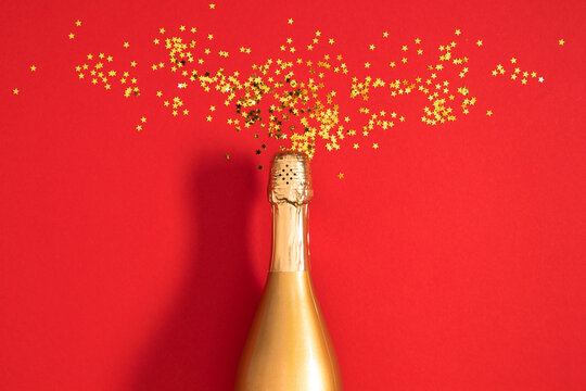 Golden champagne bottle popping with festive star shaped confetti explosion on a bright red background. Perfect for New Year and Christmas marketing, festive party invitations, holiday sale banners.