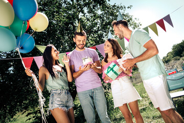 Naklejka premium Friends celebrating a birthday outdoors with cake, gifts, balloons and party hats at a sunny backyard gathering with bunting and laughter