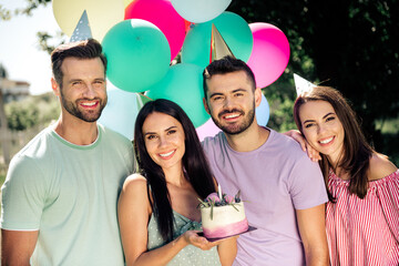 Naklejka premium Group of friends celebrating a birthday outdoors with cake, balloons and party hats, smiling young adults enjoying a summer garden celebration together