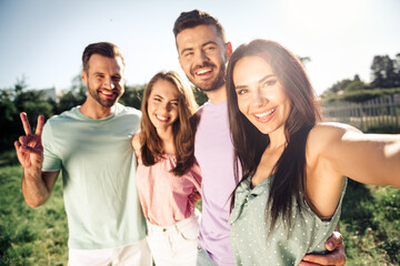 Obraz premium Four friends taking a selfie in a sunny park, smiling and happy together during a casual summer outing