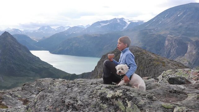 Beautiful european family with children and pet dog hiking Knutshoe summit with blue lake in mountain landscape in Jotunheimen National Park in Norway, mountains of Besseggen in background, cloudy sky
