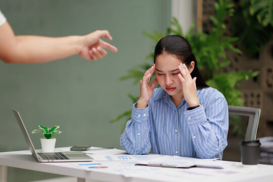 Businesswoman experiencing severe headache and workplace stress, feeling pressured by a boss pointing a finger, indicating bullying and job burnout in the office