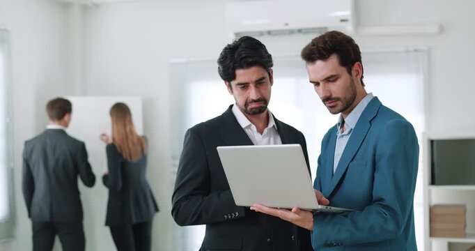 Portrait of focused bearded managers analyze marketing data on laptop in office space. Business experts monitor exchange rates on computer in company workplace