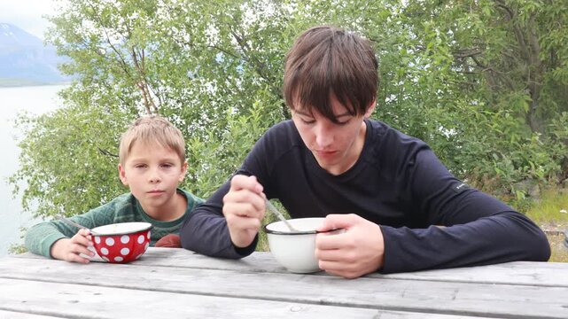 Children, boy brothers, having lunch in a reststop in Norway in beautiful nature. Kid with teddy bear eating lunch on a public wooden bench while on camping holiday in Norway