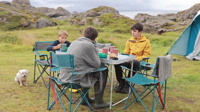 Children, boy brothers and pet dog, having breakfast in nature while wild camping in Moskenesoya, Lofoten summertime