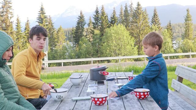 Family with children, eating dinner on a public wooden bench while on camping holiday in Lofoten, Norway