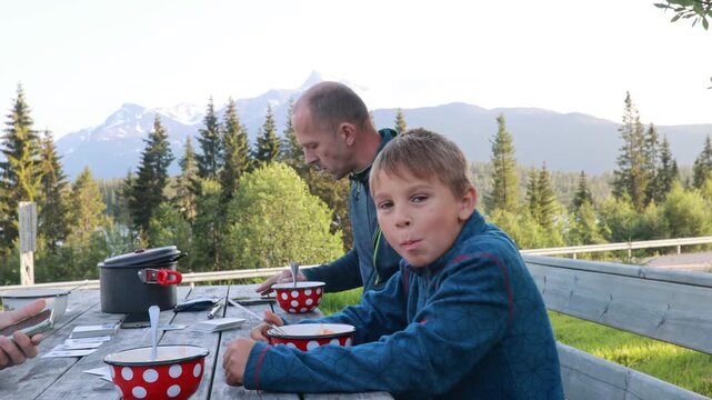 Family with children, eating dinner on a public wooden bench while on camping holiday in Lofoten, Norway
