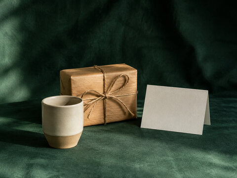 Wrapped gift box with blank card and ceramic cup on emerald fabric