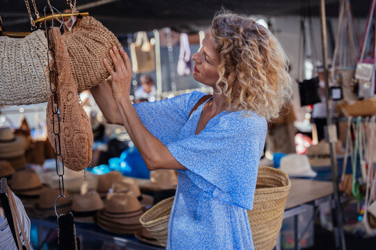 Mature Woman Examining Handmade Crochet Handbag at Traditional Outdoor Market in Spain
