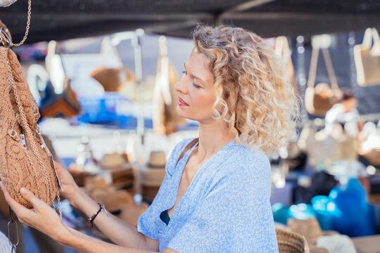 Mature Woman Examining Handmade Crochet Bag at Traditional Spanish Outdoor Market