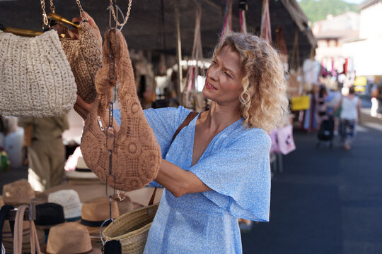 Mature Woman Choosing Handmade Crochet Bag at Local Artisan Market in Spain