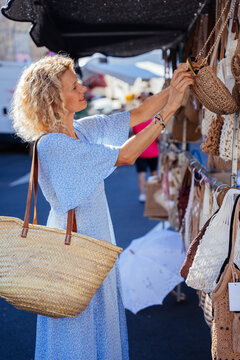 Vertical Mature Woman Browsing Handmade Crochet Bags at Traditional Spanish Street Market