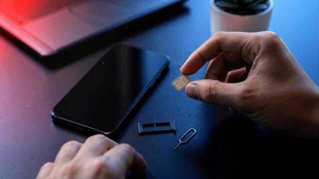 Close up of hands holding SIM card near smartphone and ejector tool. Mobile security vulnerability and SIM swap fraud concept