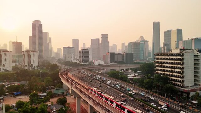 Jakarta, Indonesia - 23 July 2026: Aerial view of the Jakarta skyline with a train moving along the elevated MRT tracks above busy city traffic during sunset.