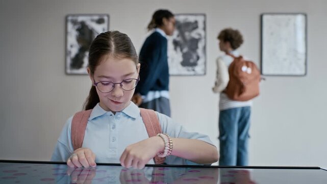 Caucasian girl wearing glasses using interactive touch screen table during museum field trip with classmates. Video is ideal for promoting modern educational technology and digital learning