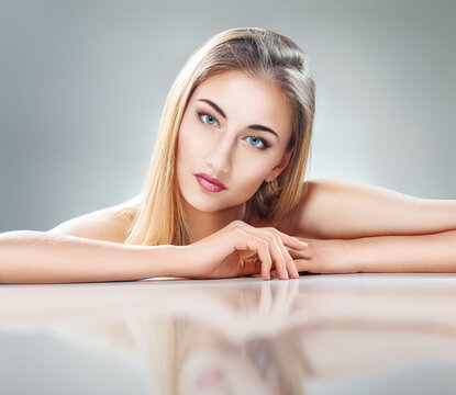 Beautiful Woman with Perfect Skin and Blue Eyes Relaxing on Reflective Surface