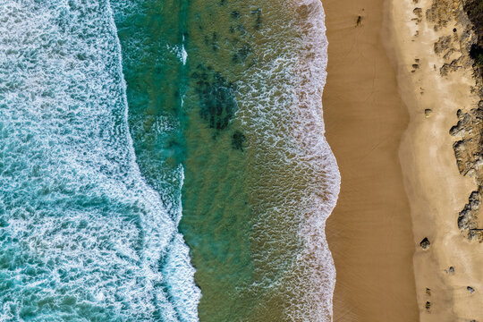 Aerial downward view of Sand Dune Beach at Brooms Head, showcasing the sandy shoreline meeting clear turquoise ocean water and the surrounding coastal dunes along the Clarence Valley coastline 