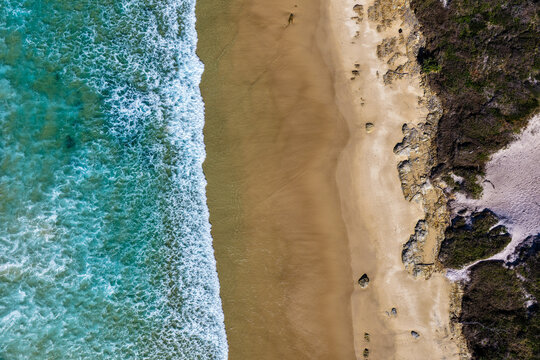 Aerial downward view of Sand Dune Beach at Brooms Head, showcasing the sandy shoreline meeting clear turquoise ocean water and the surrounding coastal dunes along the Clarence Valley coastline
