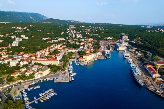 Wide aerial panorama of Kraljevica showing the historic town, marina, large harbor and shipbuilding facilities along the Adriatic coast, surrounded by densely forested hills