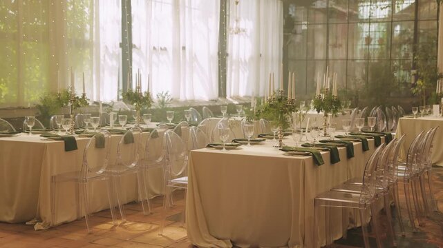 Decorated wedding tables in a bright glass venue, arranged for a romantic celebration and reception.
